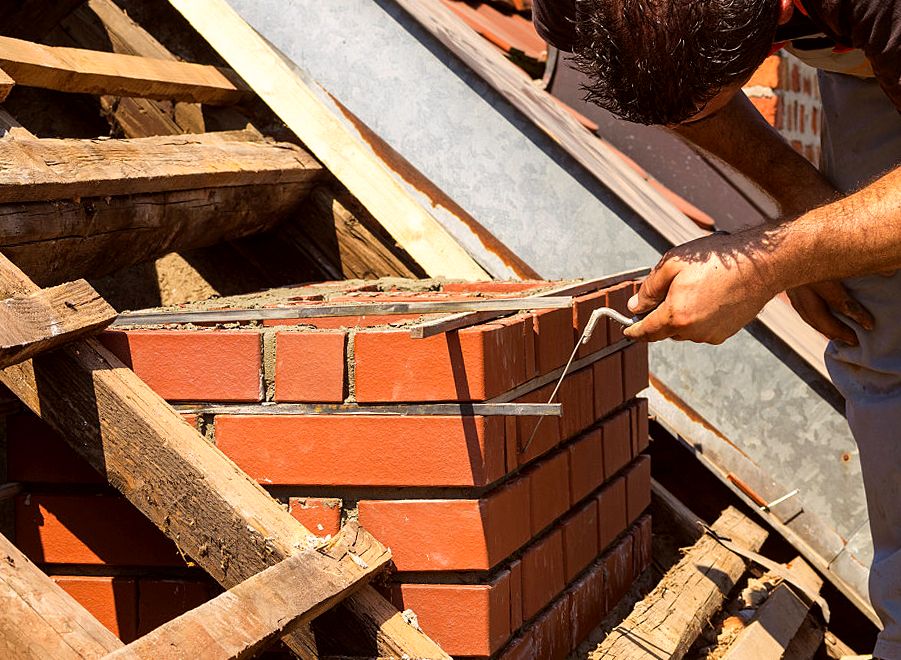 Mason laying fresh brick courses for a chimney between roof rafters